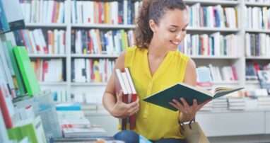 A person surrounded by full bookshelves reads a book.