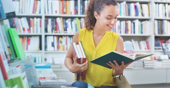 A person surrounded by full bookshelves reads a book.