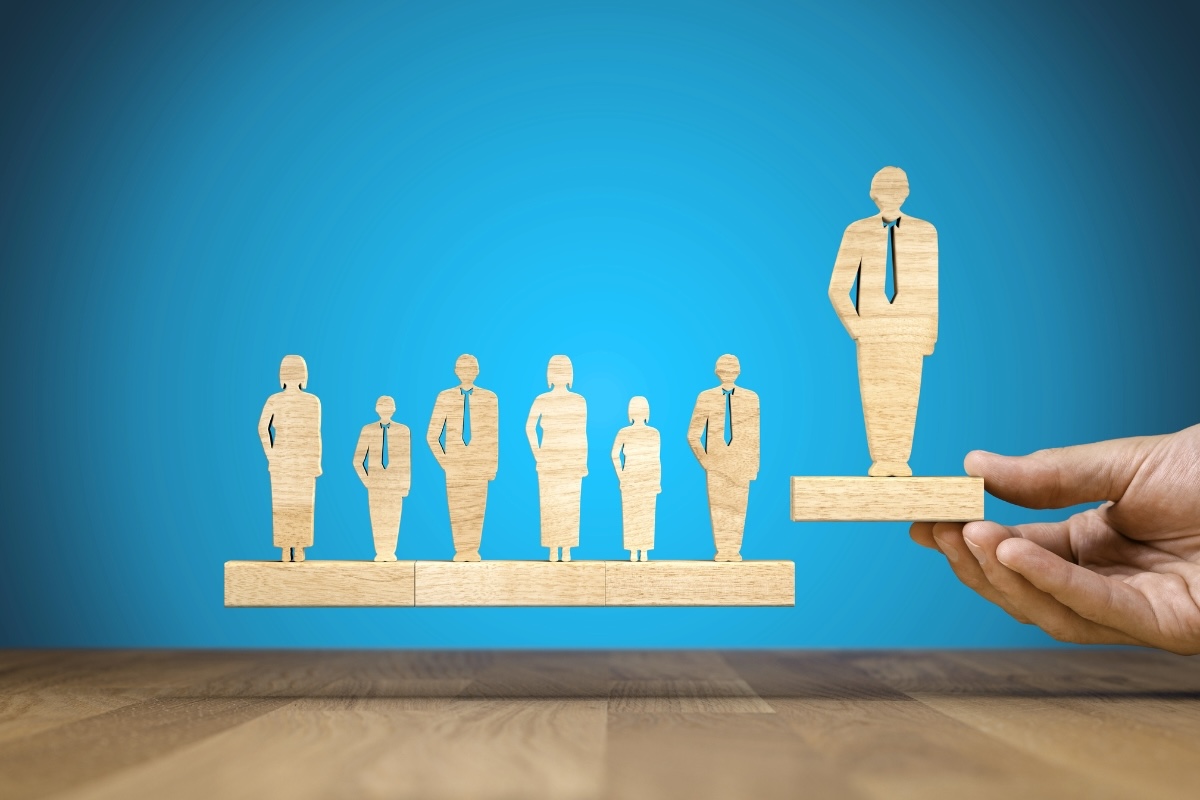A hand picks up a wooden cutout of a person from a line of 7 wooden cutouts
