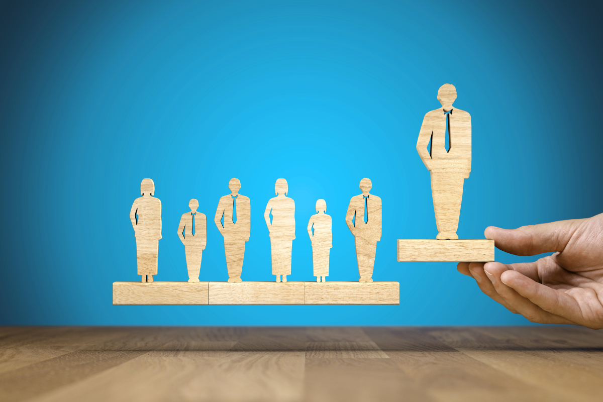 A hand picks up a wooden cutout of a person from a line of 7 wooden cutouts