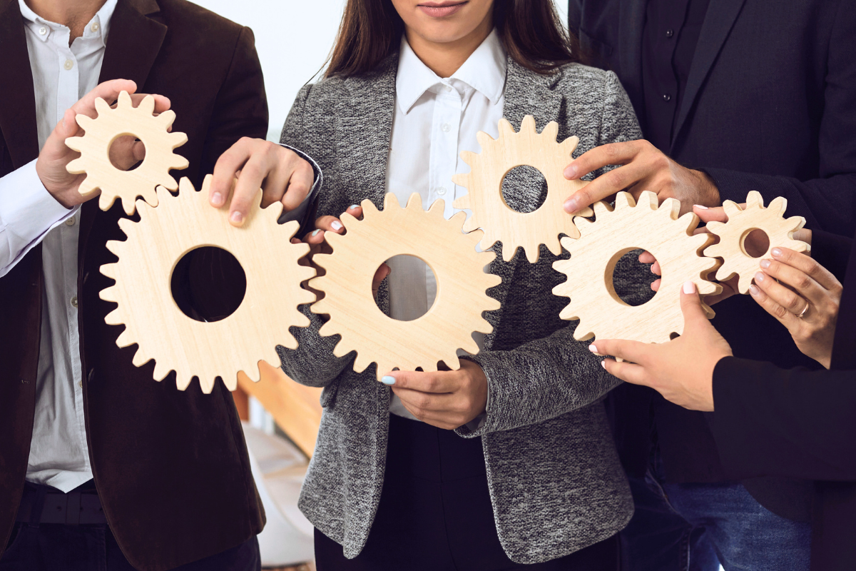 Four business people hold up and connect wooden gears