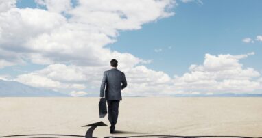 A business person walks through a desert with an arrow pointing the way