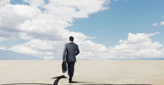 A business person walks through a desert with an arrow pointing the way