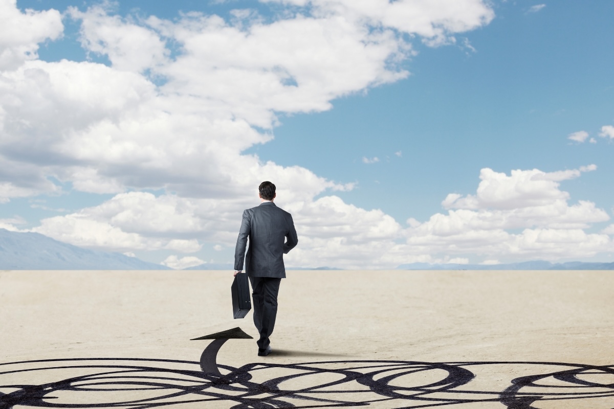 A business person walks through a desert with an arrow pointing the way