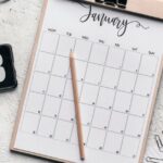 A calendar on a desk cluttered with paperclips, a stapler, a clock, and headphones