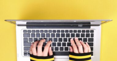 A person typing on a laptop on a yellow background