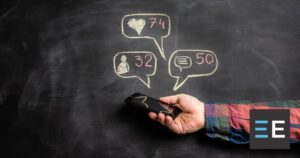 A person holding a smartphone. In chalk on the wall behind it are speech bubbles with likes, comments, and followers symbols