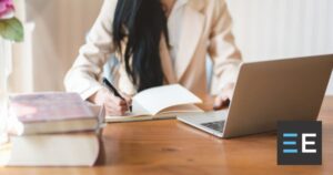 A person at a desk working on a laptop and taking notes