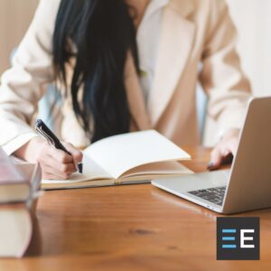 A person at a desk working on a laptop and taking notes