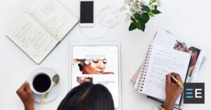 A person at a cluttered desk looking at a beauty blog on a tablet
