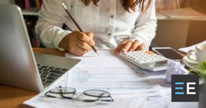 A person at a desk covered in paper using a calculator and a pencil