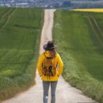 A person wearing a hat and backpack standing at the beginning of a long, straight path