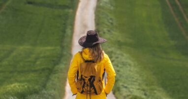 A person wearing a hat and backpack standing at the beginning of a long, straight path