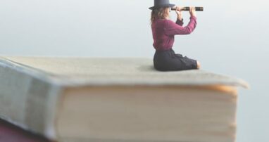 A small person looking through a spyglass seated atop a stack of books