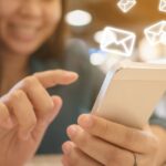A person using their smartphone. Around it are email icons
